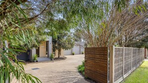Une allée pavée mène à un bâtiment moderne, entouré d’une clôture en bois et agrémenté de verdure.