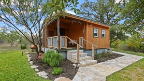 A rustic cabin with a porch, stone steps, and a small garden. - Fredericksburg, TX Cabin - River Access - Romantic Getaway (Fredericksburg)
