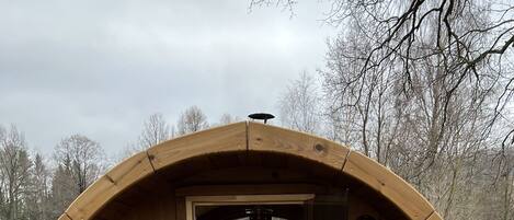 A wooden barrel-shaped structure with a fireplace, benches, and a wooden deck.