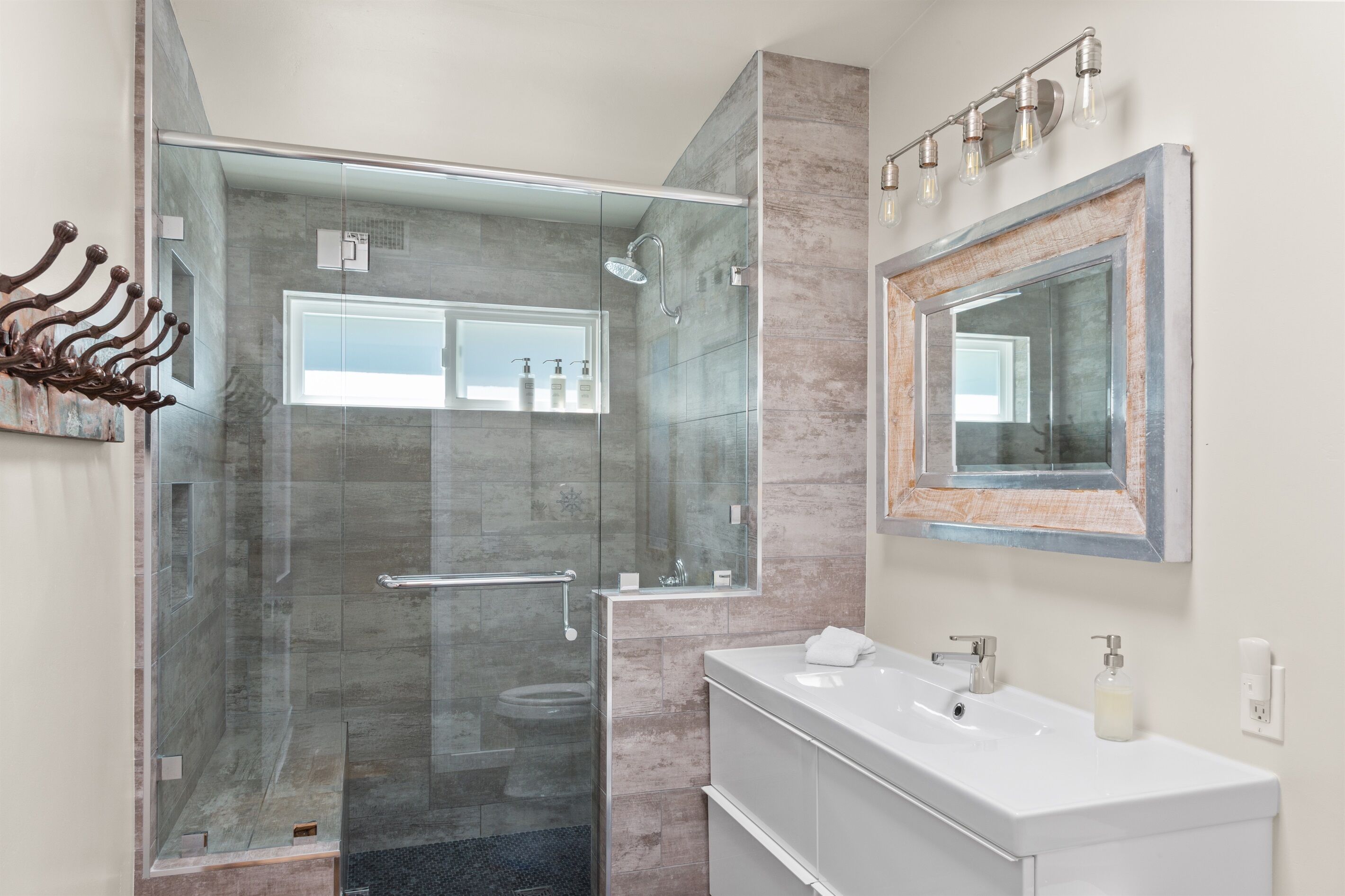 Un baño moderno con cabina de ducha de vidrio, un espejo grande y un tocador blanco con lavabo.