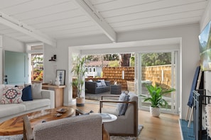 A spacious living room with a large sliding glass door leading to a backyard. There is a sofa, a coffee table, and a chair.