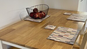Una mesa de comedor con una cesta de metal para frutas, individuales y sillas blancas.