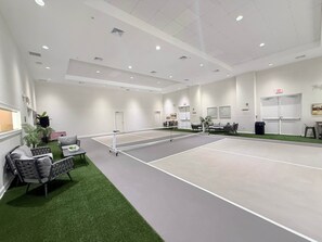 Un court de tennis avec un filet, entouré de sièges et d’une petite table.