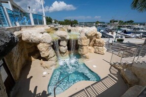 Zona de piscina con cascada, rodeada por un puerto deportivo y barcos.