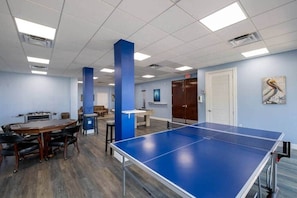 A room with a ping pong table, a wooden table with chairs, and a blue pillar. - Oceanview • Pool View • Indoor/Outdoor Pickleball (Key Largo)