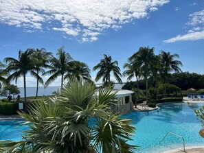 Zona de piscina con palmeras, un pabellón y vista al océano.