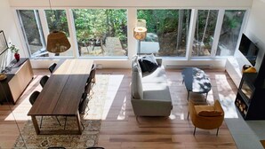 A modern living room with a dining area, large windows, and a fireplace. - Lakefront cottage in the Laurentians (Saint-Adolphe-d'Howard)