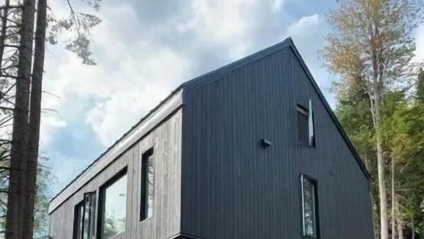 A modern two-story house with a sloped roof, large windows, and a wooden deck. - Lakefront cottage in the Laurentians (Saint-Adolphe-d'Howard)
