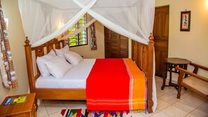 A four-poster bed with white linens, a red and orange blanket, and a wooden headboard. - Charming 1-bed Cottage in Diani Beach 10min to bea (Diani Beach)