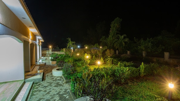 Vue nocturne d'une cour avec un chemin pavé, des sièges extérieurs et des luminaires décoratifs éclairant le jardin.