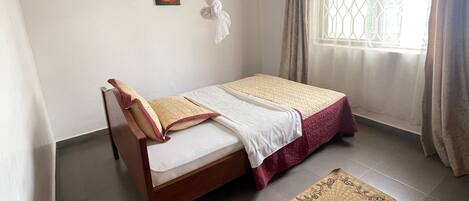 A bedroom with a bed, a bedside table, a window with curtains, and a wall-mounted air conditioning unit.