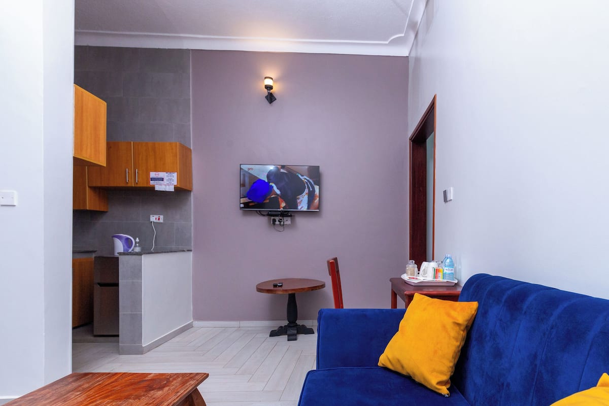 Ein Wohnzimmer mit einem blauen Sofa, einem kleinen runden Tisch und einem an der Wand befestigten Fernseher.