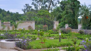 Un jardin aménagé avec une fontaine centrale, entouré de différentes plantes et d’une porte en métal.