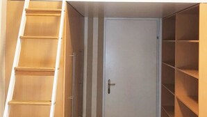 Habitación compacta con cama entrepiso integrada, una puerta que da a un armario y una escalera de madera para acceder.