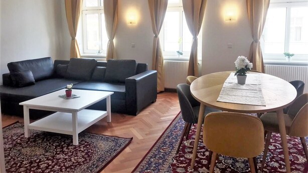 Una sala de estar moderna con un sofá, una mesa de centro, una mesa de comedor con sillas y una alfombra estampada.