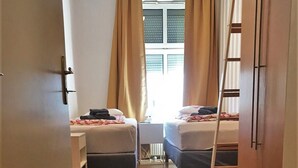 Una habitación de hotel con dos camas, una ventana con cortinas, un radiador y suelo de madera.