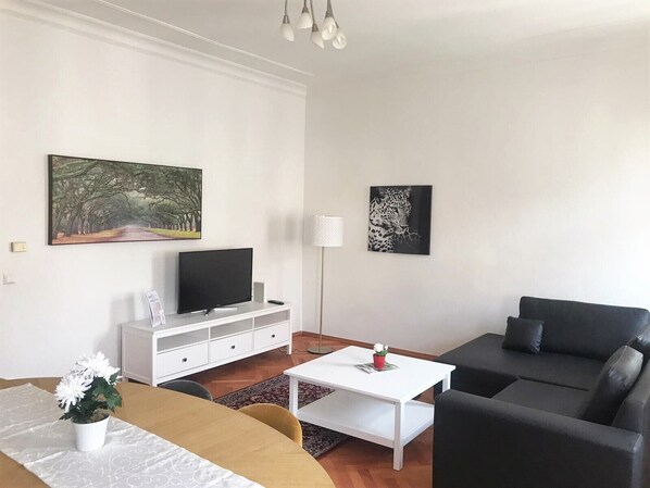 Uma sala de estar moderna com um sofá, uma mesa de centro, uma televisão e obras de arte nas paredes.