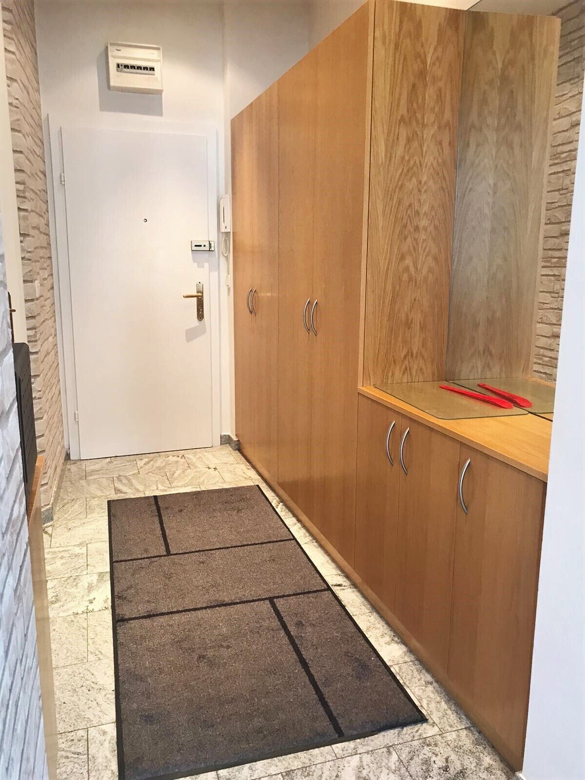 Ein Flur mit einem Holzschrank, einer Fußmatte und einer Wand-Klimaanlage.