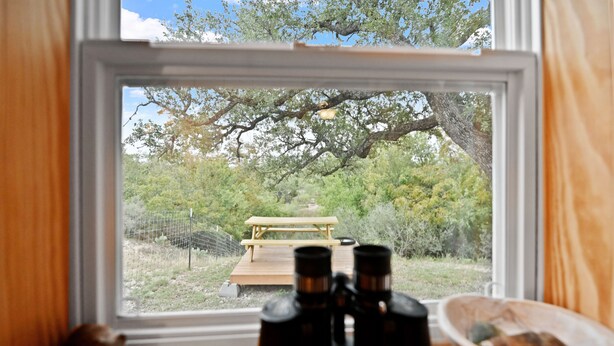 Una finestra, binocoli su un tavolo, una panca di legno e una ciotola.