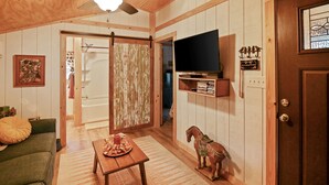Una camera accogliente con soffitto in legno, una ventola a soffitto, un televisore a schermo piatto montato al muro, una porta in legno e una piccola decorazione a forma di cavallo di legno.