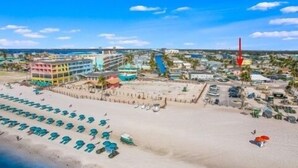 An aerial view of a beach with rows of sun loungers, a building with multiple balconies, and a red flag indicating a warning or caution. - 122 Primo Dr 3 Bedroom Home by RedAwning (Fort Myers Beach)