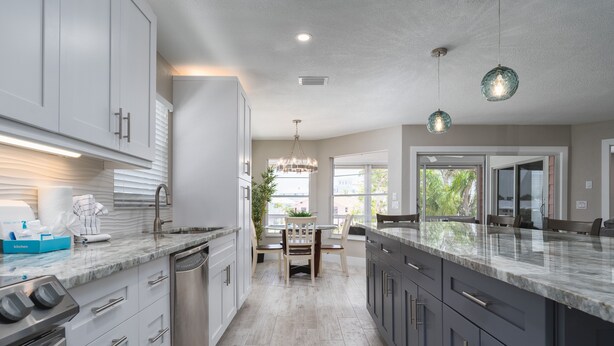 A modern kitchen with a central island, built-in appliances, and a dining area with a view. - 122 Primo Dr 3 Bedroom Home by RedAwning (Fort Myers Beach)