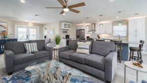 A modern living room with two grey sofas, a coffee table, and a ceiling fan. - 122 Primo Dr 3 Bedroom Home by RedAwning (Fort Myers Beach)