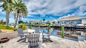 Un patio frente al agua con sillas Adirondack, una fogata y vistas al puerto deportivo.