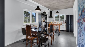 A modern kitchen with a dining area, large windows, and a view of the outdoors.