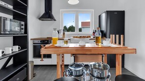 A modern kitchen with a wooden table set for breakfast, a black refrigerator, and a window with a view of a red-roofed building.