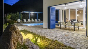 A modern outdoor pool area with lounge chairs, a dining table, and a covered seating area.