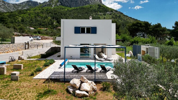 A modern villa with a swimming pool, outdoor seating, and a mountain backdrop.