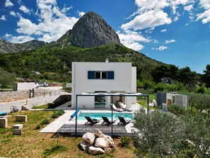 Una villa moderna con piscina, mobiliario exterior y montañas al fondo.