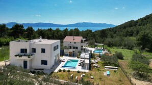 A modern villa with a swimming pool, surrounded by lush greenery and a view of the sea.