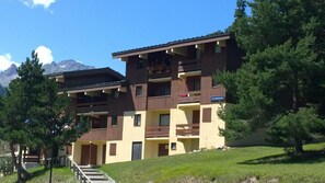 Un edificio de varios pisos con balcones, un letrero que dice “LES CAMPANIES” y un paisaje montañoso al fondo.