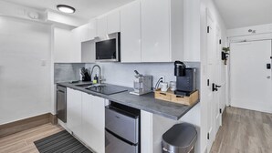 A modern kitchen with white cabinetry, a built-in microwave, a coffee maker, and a dishwasher. - Beachfront Remodeled Studio in Daytona Beach with King-Size Bed (Daytona Beach)