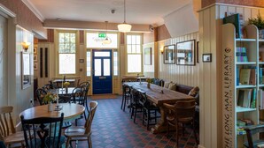 A dining area with multiple tables and chairs, a blue door, and a bookshelf labeled "The Long Man Library." - Long Man Inn (Polegate)