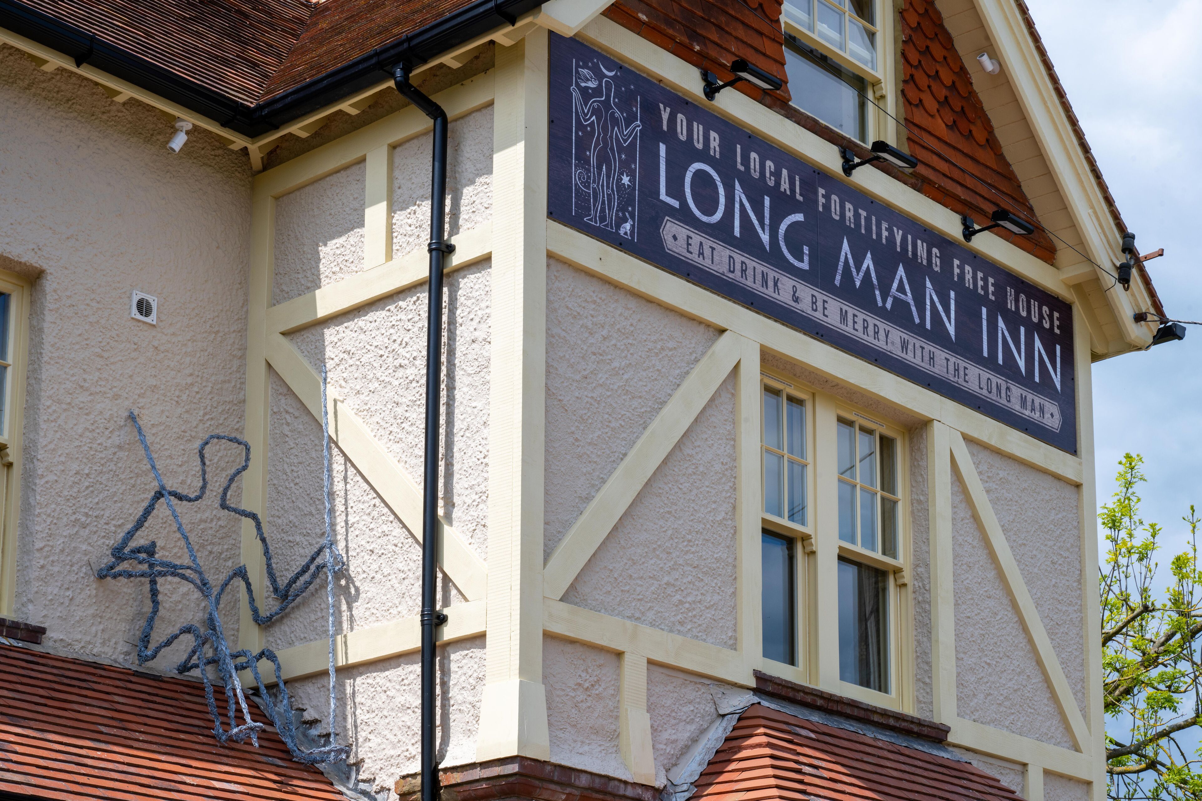 A building with a sign that reads "Your Local Fortifying Free House Long Man Inn" and mentions "Eat Drink Berry With The Long Man."