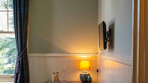 A cozy room with a bed, a desk with a lamp, a chair, a small cabinet, and a window with curtains. - Long Man Inn (Polegate)