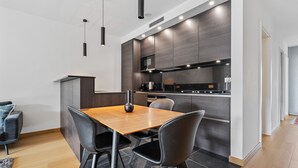 A modern kitchen with dark wood cabinets, a wooden dining table, and black chairs. - Stylish Apt in Cloche dOr w balconyID233 (Luxembourg City)