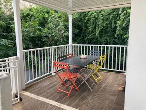 Une terrasse extérieure couverte, dotée d’un plancher en bois, d’une balustrade blanche et d’une table avec des chaises.