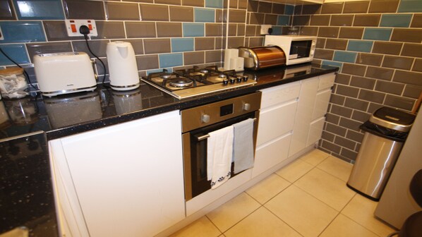 Kitchen area with gas stove, microwave, toaster, sink, and trash bin.