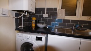 Compact laundry area with a front-loading washing machine, stainless steel sink, and tiled backsplash.
