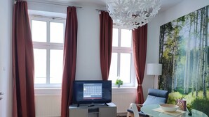Moderni olohuone, jossa on televisio, lasipöytä ja seinällä suuri metsäaiheinen seinämaalaus.