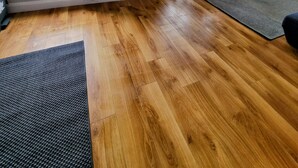 Ein großzügiger Wohnraum mit Holzboden, großen Fenstern mit Vorhängen, einem wandmontierten Flachbildfernseher und einem kleinen Tisch mit Stühlen.
