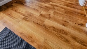 Ein modernes Wohnzimmer mit Holzboden, einer Couch, einem Fernseher und einem Essbereich mit Tisch und Stühlen.