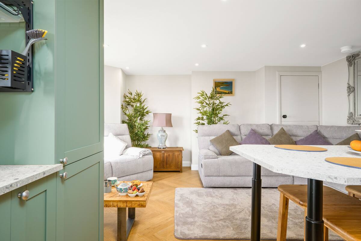 A modern living room with a sofa, a small table with snacks, a lamp, and two potted plants.