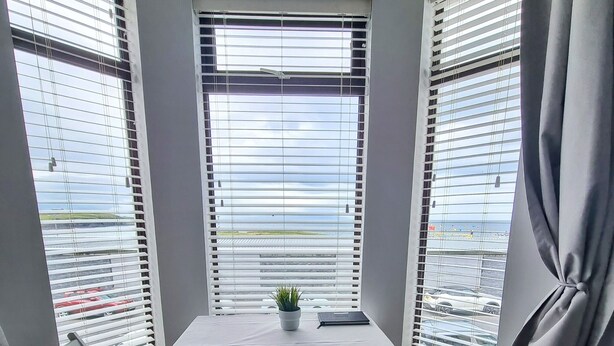 Ein Zimmer mit einem Couchtisch in der Ecke, weißen Stühlen, einer kleinen Topfpflanze und Blick durch Jalousien.