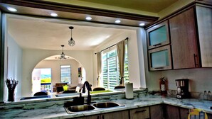 A kitchen with a marble countertop, wooden cabinets, and a view into the living area. - Lola's DonJon + Peaceful prop. + Near Beaches + HTUB (San German)