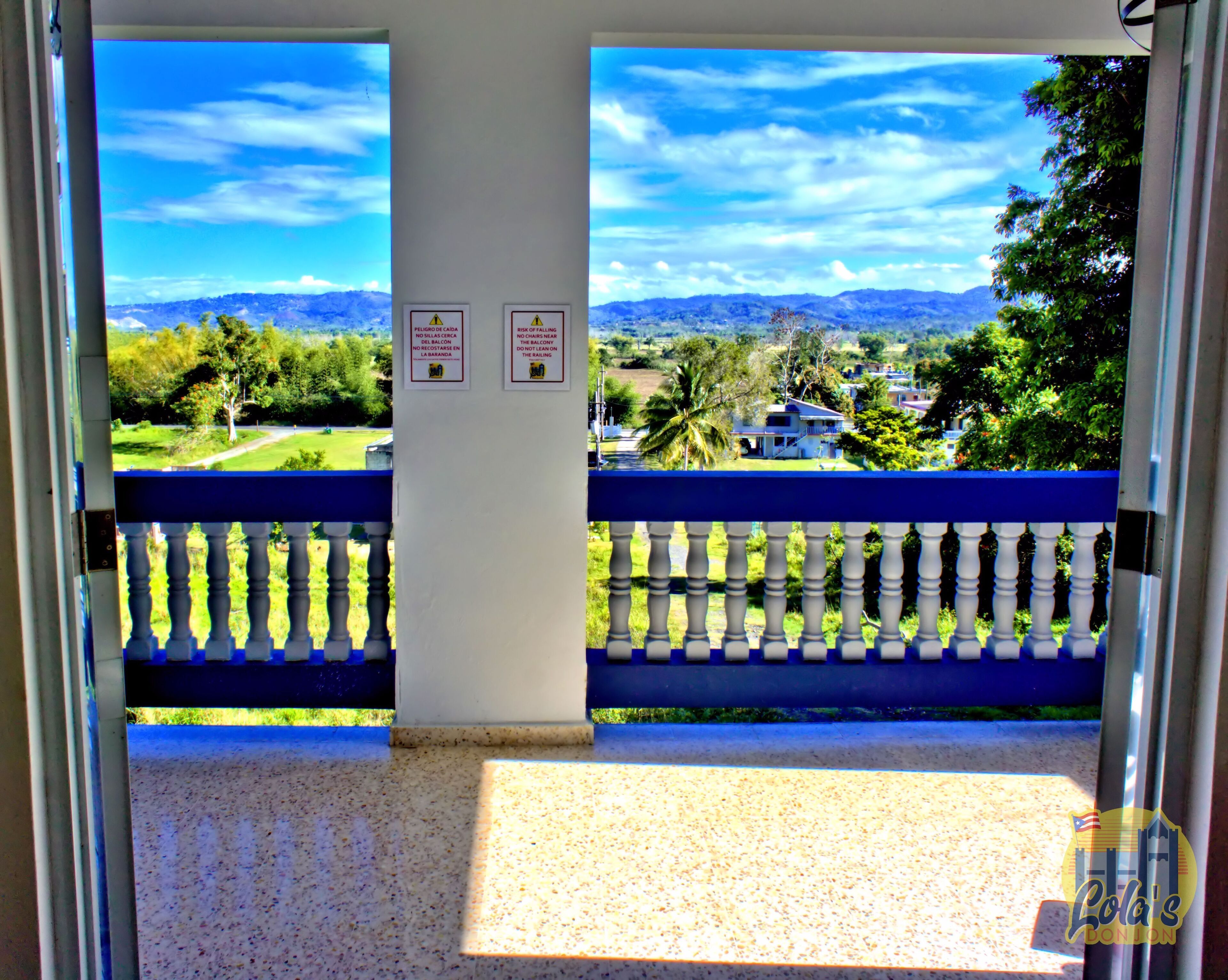 A balcony with a view of a mountainous landscape, two warning signs, and a blue railing.